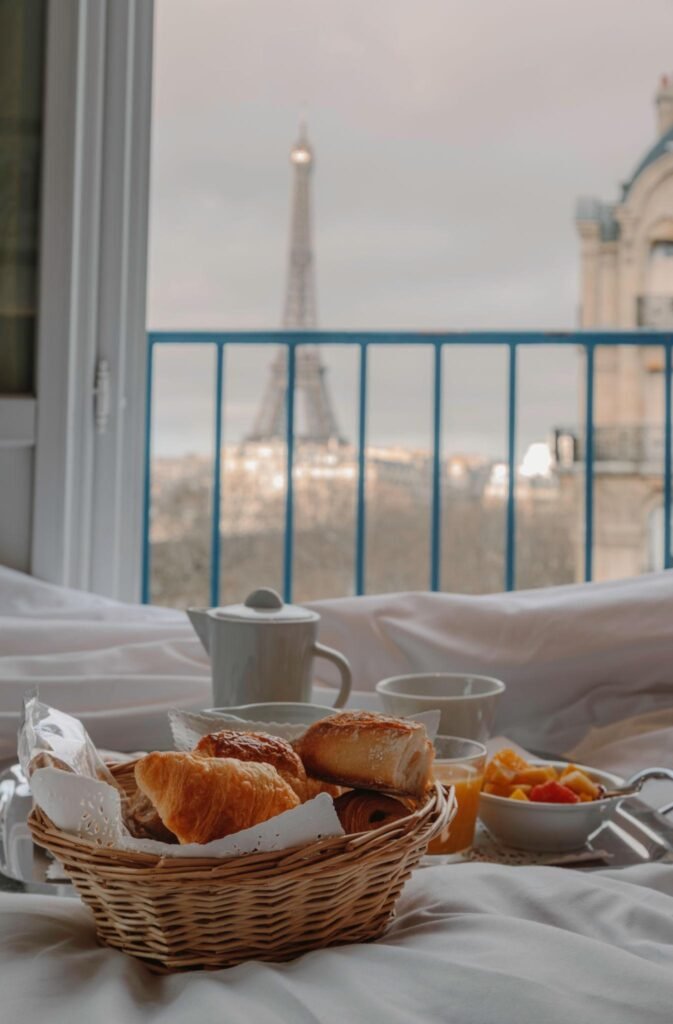 Two cups of coffee and croissants beside a bright Paris-inspired balcony view.